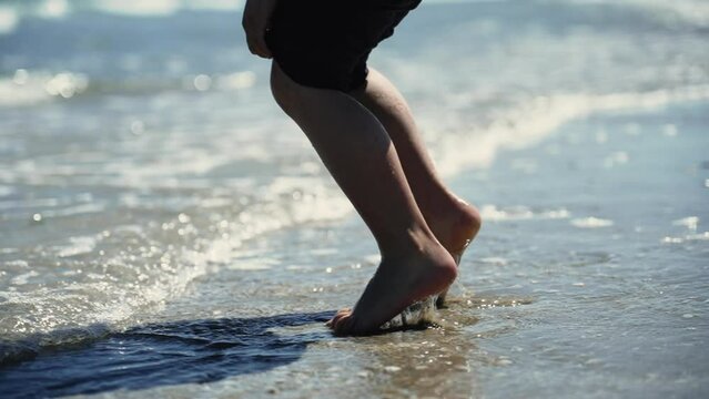 Happy child legs jumping at beach water in super slow motion. Kid feet walking outdoors feeling sand barefeet