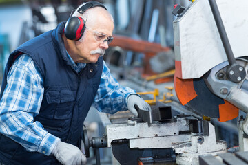 elderly worker watches processing of detail on milling machine