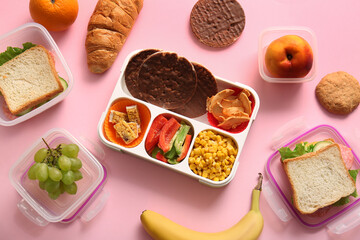 Lunchboxes with different delicious food on pink background