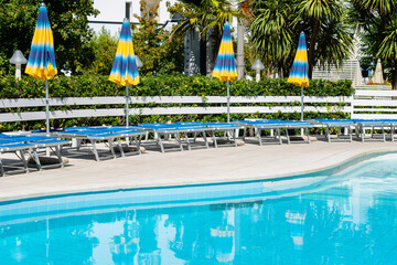 Grab bars ladder in the blue swimming pool, empty chaise longue, private swimming pool near hotel