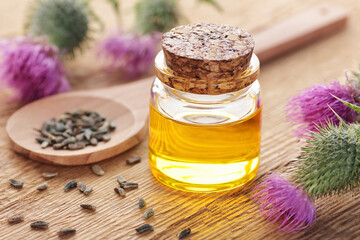 Thistle oil in glass bottle with seeds and flowers on wooden rustic background, closeup, natural medicine, skin care, healthy food supplement, immune health concept