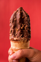 Hand taking chocolate ice cream cone on red background with copy space 