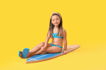 Little Asian girl with surfboard on yellow background