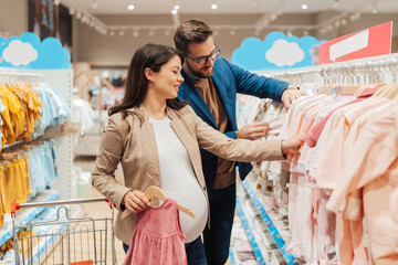 Attractive middle age couple enjoying in buying clothes and appliances for their new baby. Heterosexual couple in baby shop or store. Expecting baby concept.
