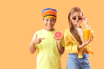 Little children with bottle of fresh citrus juice and grapefruit slice on orange background