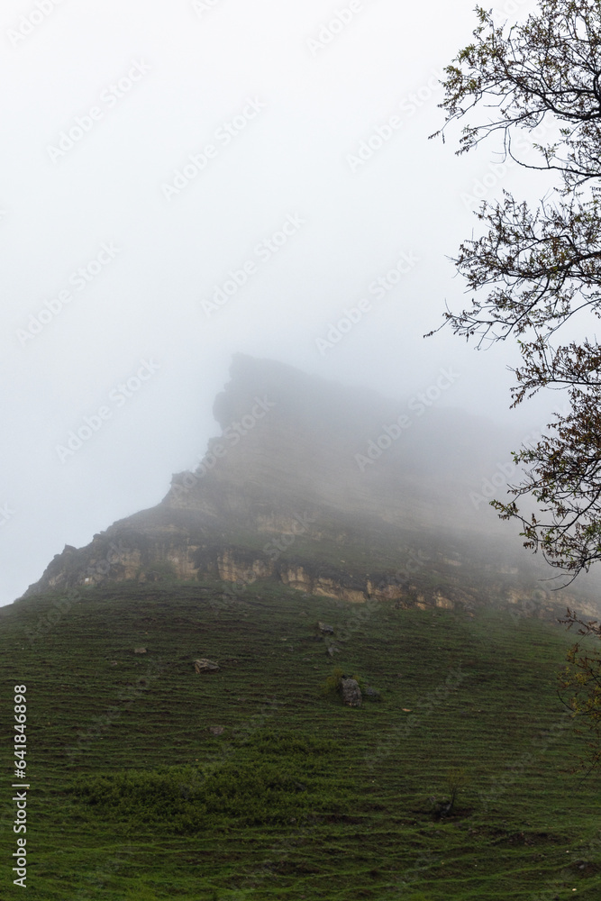 Wall mural Mountain peak is under cloudy sky on a foggy day