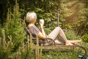 Mature romantic woman holding a cup of coffee  in garden relax bed