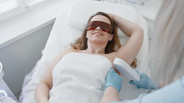 A woman in a beauty salon trusts a cosmetologist during the photoepilation procedure, feeling comfortable and caring. The beautician in the clinic guarantees the safety and effectiveness of laser hair