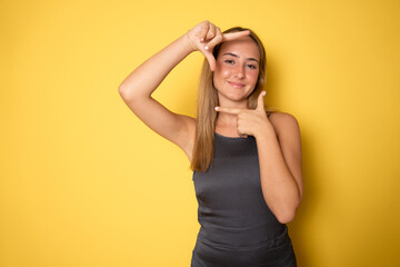 Picture of lovely woman creating a frame with fingers isolated on yellow background