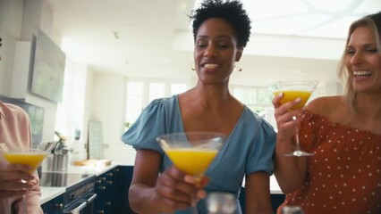 Three mature female friends at home having fun making a toast with and drinking cocktails together - shot in slow motion