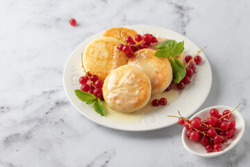 Cottage cheese pancakes or syrniki with red currant and milk sauce on white plate marble background, closeup view. Russian, Ukrainian cuisine. Healthy tasty breakfast