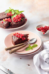 A piece of chocolate cake brownie decorated with red currant berries and mint on white marble table