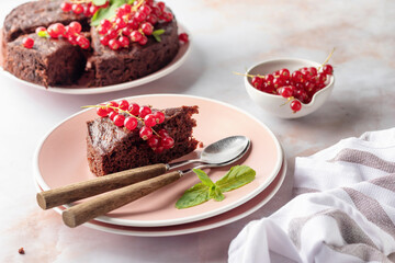 A piece of chocolate cake brownie decorated with red currant berries and mint on white marble table