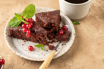 Two pieces of chocolate cake brownie close up decorated with red currant berries and mint for coffee on beige textured background