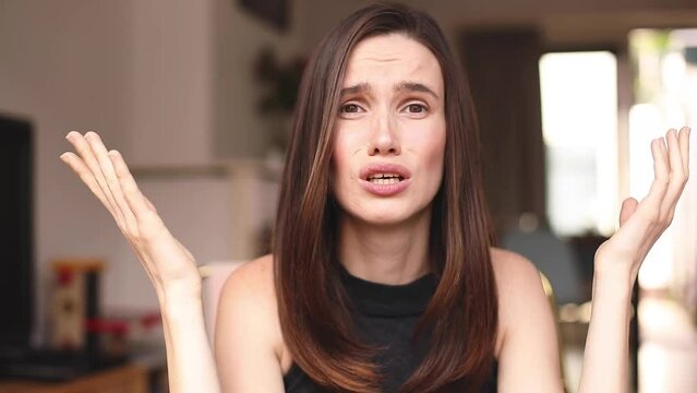 Girl raising her hands, waiting for excusement sitting at home. Woman asking why. Upset young confused woman, is not understanding anything. Angry irritated woman spreading hands, feeling rage anger.