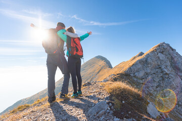 Fantastic view of a hiker couple standing on a ridge celebrating success with spread arms,...