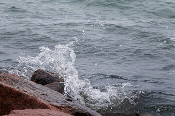 Close-up of splash of a small wave crashing on rocks.