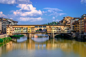 Ponte Vecchio (old Bridge) in Florence, Italy. This medieval stone bridge that spans river Arno, consists of three segmental arches and it has always hosted shops and merchants. - obrazy, fototapety, plakaty