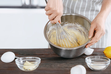 A cook in an apron kneads the dough in a bowl using a whisk for baking bread, dessert, pie, buns....