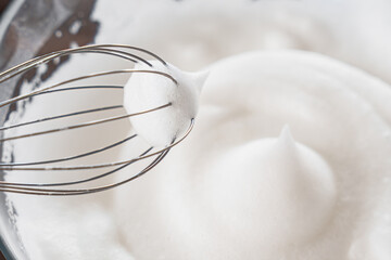 Close-up of a whisk and beaten egg whites to stiff peaks, a step in the preparation of breakfast...
