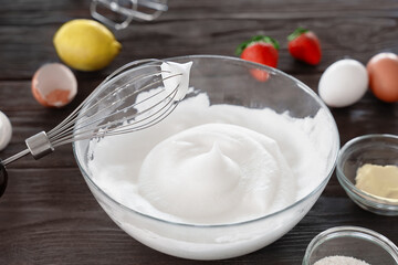 Close-up of a whisk and whipped egg whites to stiff peaks, a step in the preparation of breakfast dough or tender pancakes. White whipped foam of egg whites, bakery preparation. Wooden table.