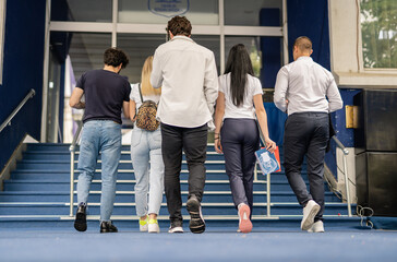Five students walking up staircase in front of university. Back view photo