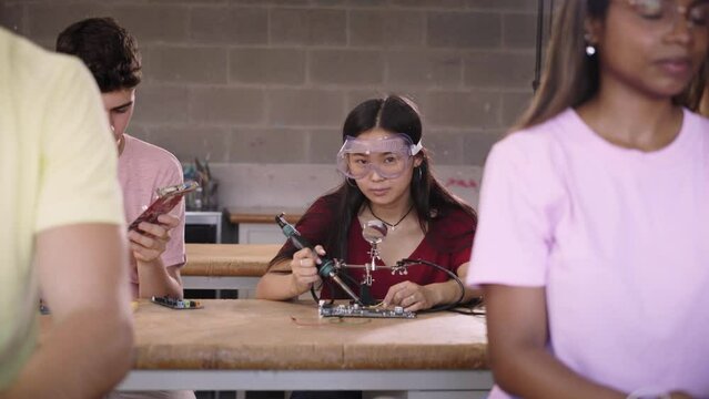 A group of students at a technical college are in the classroom studying by practicing soldering hardware parts on circuit boards. Superior engineering, concept development and innovation.