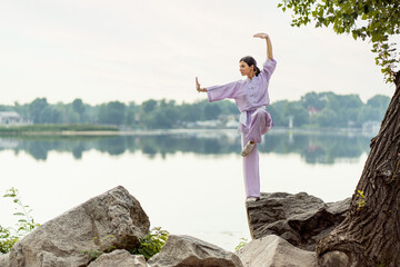 Serious woman, kungfu master  wearing kimono training, practicing wushu standing on stone near...