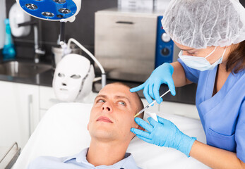Portrait of male client of aesthetic cosmetology clinic during procedure of face mesotherapy. Male skin care concept..