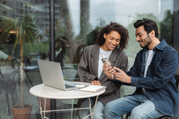 Confident smiling businesspeople looking at the smartphone screen, working, using laptop