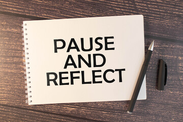 PAUSE AND REFLECT text on sticker on diary with keyboard and pencil.