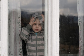Little grimy boy looking through a dirty old window. He holds his head in his hands excitedly.