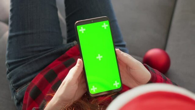A woman with a smartphone and a good mood is preparing for holiday shopping and ordering gifts online in cozy home environment. Preparing for new year and Christmas. Futage chromakey and green screen