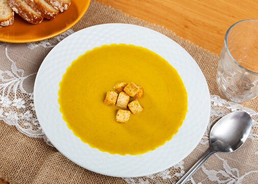Carrot cream with pieces of croutons served in a plate with spoon and other table appointments