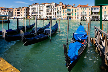 Fototapeta na wymiar Traditional Venetian gondolas moored to pier in Grand Canal on background with old colorful architecture of central districts of Venice