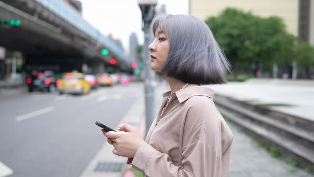 台湾台北の大通りでスマートフォンを操作しながらタクシーを待つ女性 A woman waits for a cab on a main street in Taipei, Taiwan, while operating a smartphone.