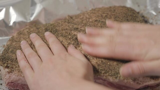 This video shows a pair of hands rubbing in seasonings on a large piece of raw meat.
