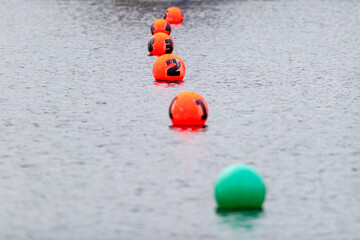 A row of orange colored buoys at the finish line of a boating race. The plastic buoys are numbered...