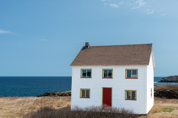 A white saltbox traditional-style house on the edge of the coastline overlooking the blue ocean and...