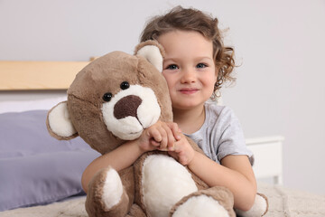 Cute little girl with teddy bear on bed indoors