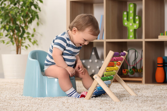 Little child with abacus sitting on plastic baby potty indoors
