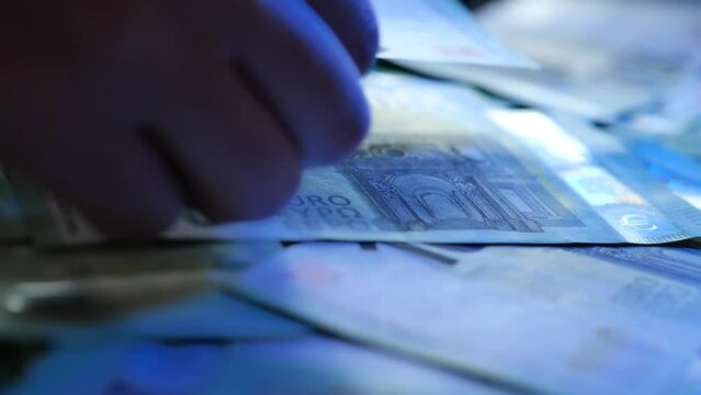 Euro money. Hands raking euro bills in blue light in a dark room. Money crimes.Cash settlement. 4k footage