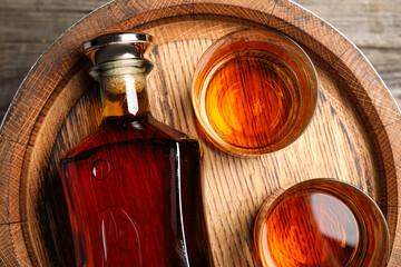 Glasses and bottle of whiskey on wooden barrel, flat lay