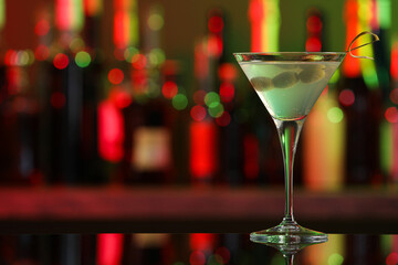 Martini glass with cocktail and olives on counter in bar. Space for text