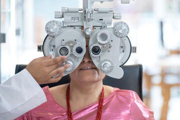 Middle-aged Indian or Nepali woman looking through Optical Phoropter during eye exam, with an optometrist nearby, diagnostic ophthalmology 