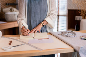 Asian tailor women creative and designing new fashion collection while drawing sketch in notebook