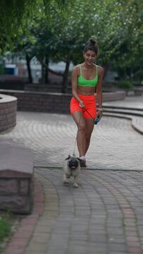 Sporting a smile, a lovely girl in athletic attire enjoys a walk with her pug dog through the city streets.