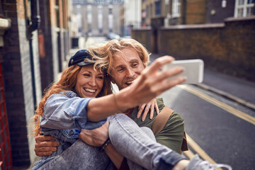 Young couple walking down a city street and using a smart phone to take a selfie in London , UK