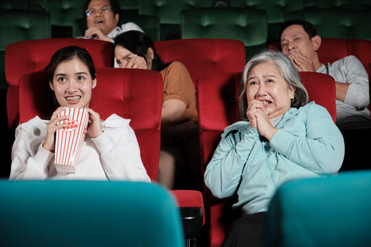 Various people in theater. Asian senior woman and many audiences are scared of watching thriller and horror cinema, frightened together on movie stage, and entertainment lifestyle with film show. - Powered by Adobe