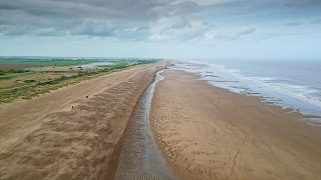 Aerial video footage of a coastal beach scene with ocean, sand dunes and crashing waves